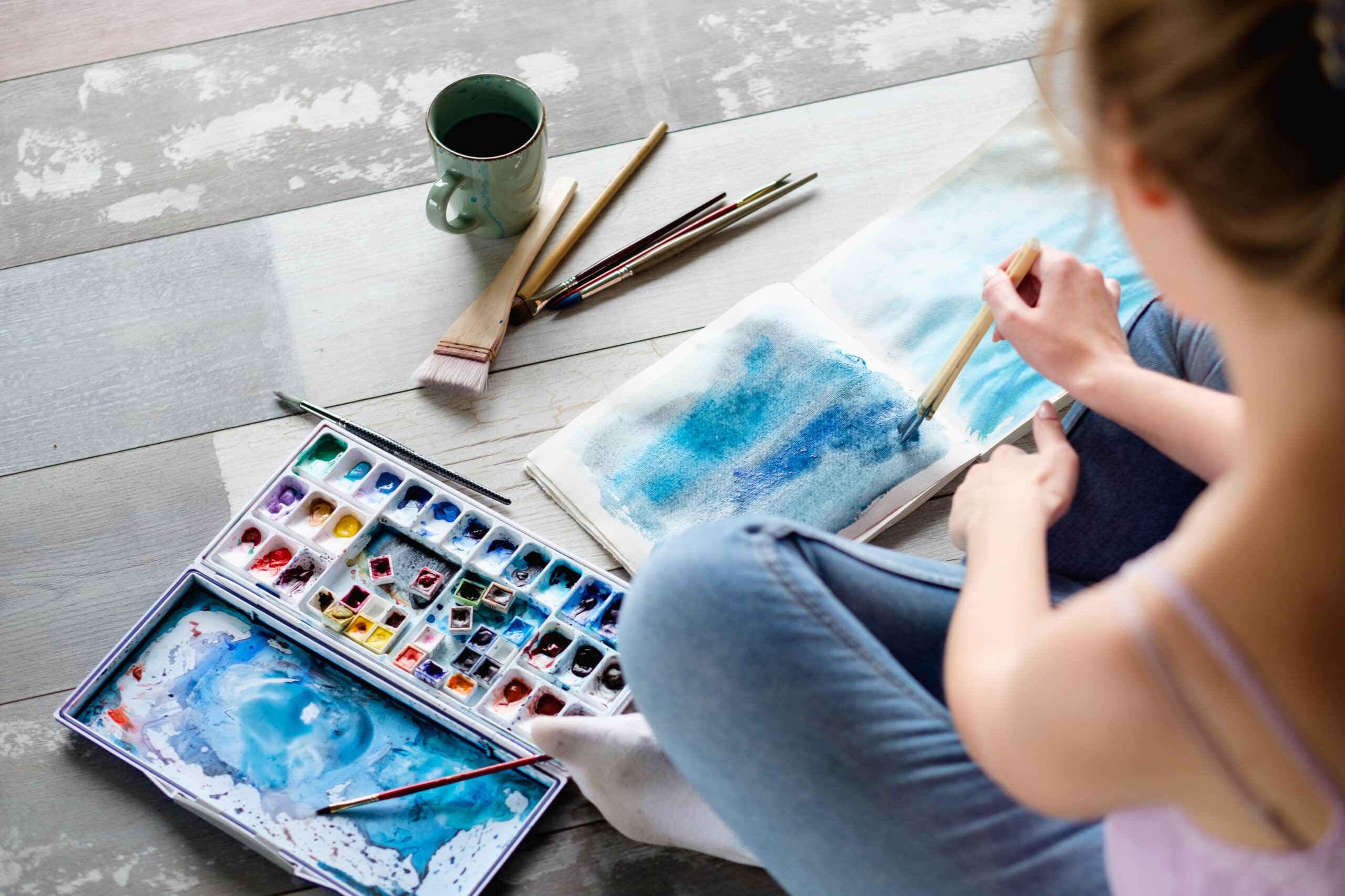 woman practicing expressive art therapy by painting with watercolors on the floor