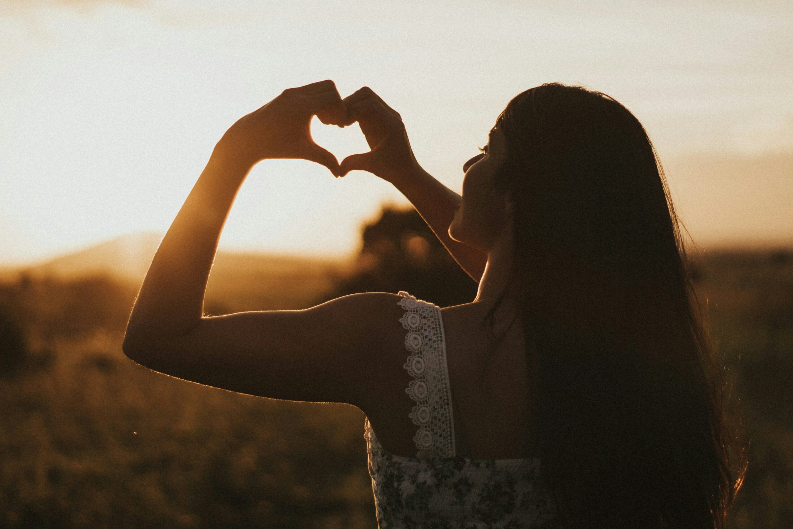 woman with her hands in the shape of a heart, in the sunset