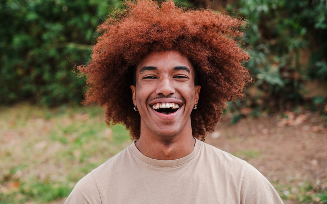 Close up portrait of young african american toothy man with afro hair smiling looking at camera outdoors. Head shot of a glad teenager boy laughing with friendly and carefree attitude. High quality photo - Joy