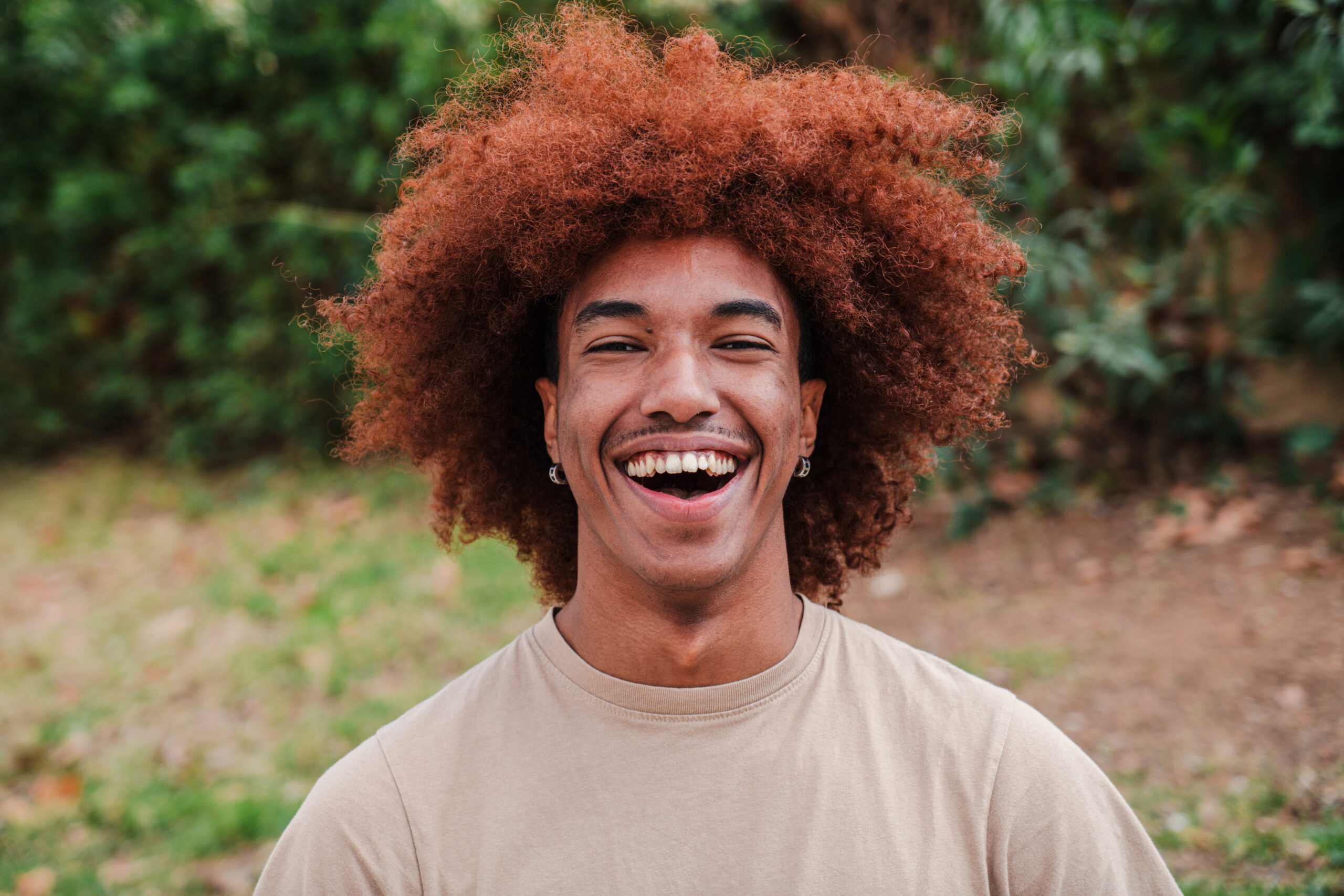 Close up portrait of young african american toothy man with afro hair smiling looking at camera outdoors. Head shot of a glad teenager boy laughing with friendly and carefree attitude. High quality photo - Joy