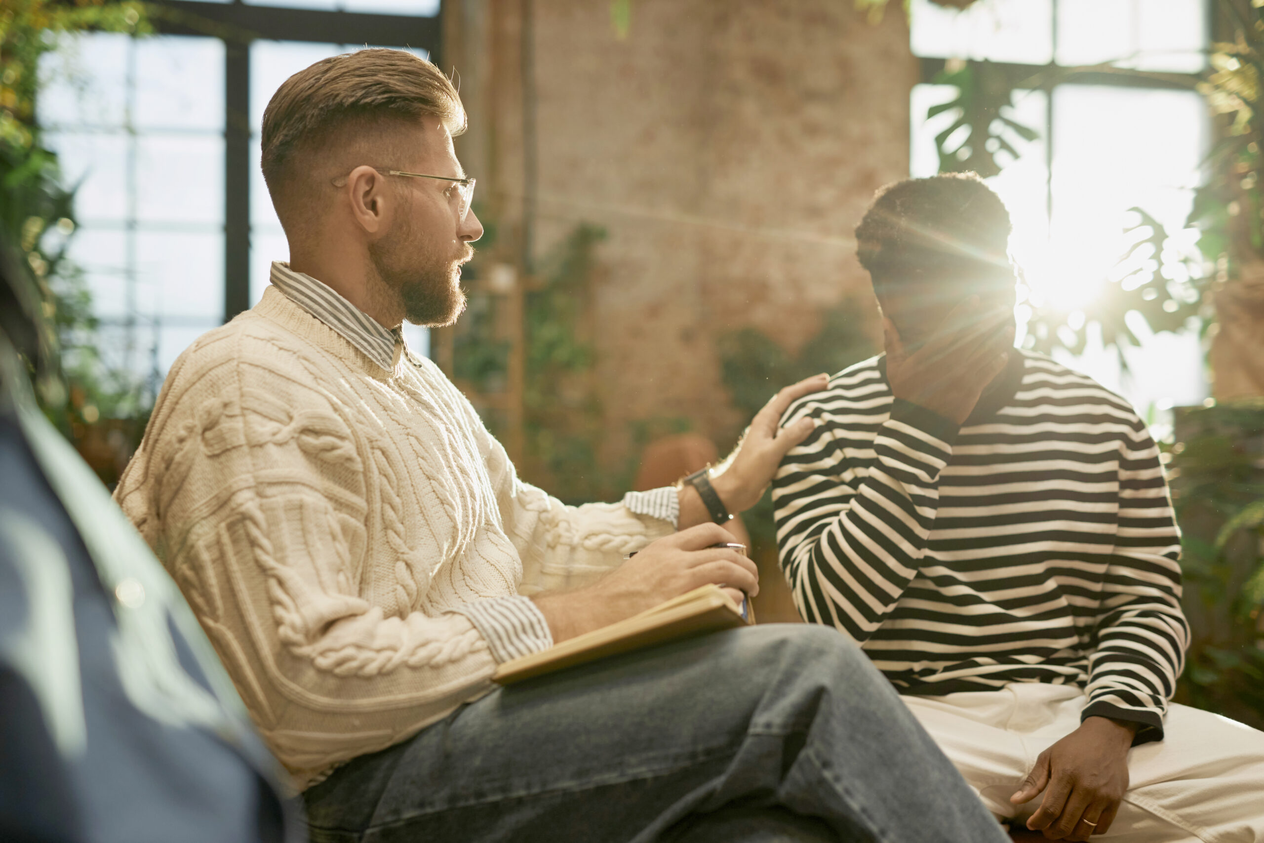 Side view portrait of bearded male psychologist supporting client during therapy session with lens flare